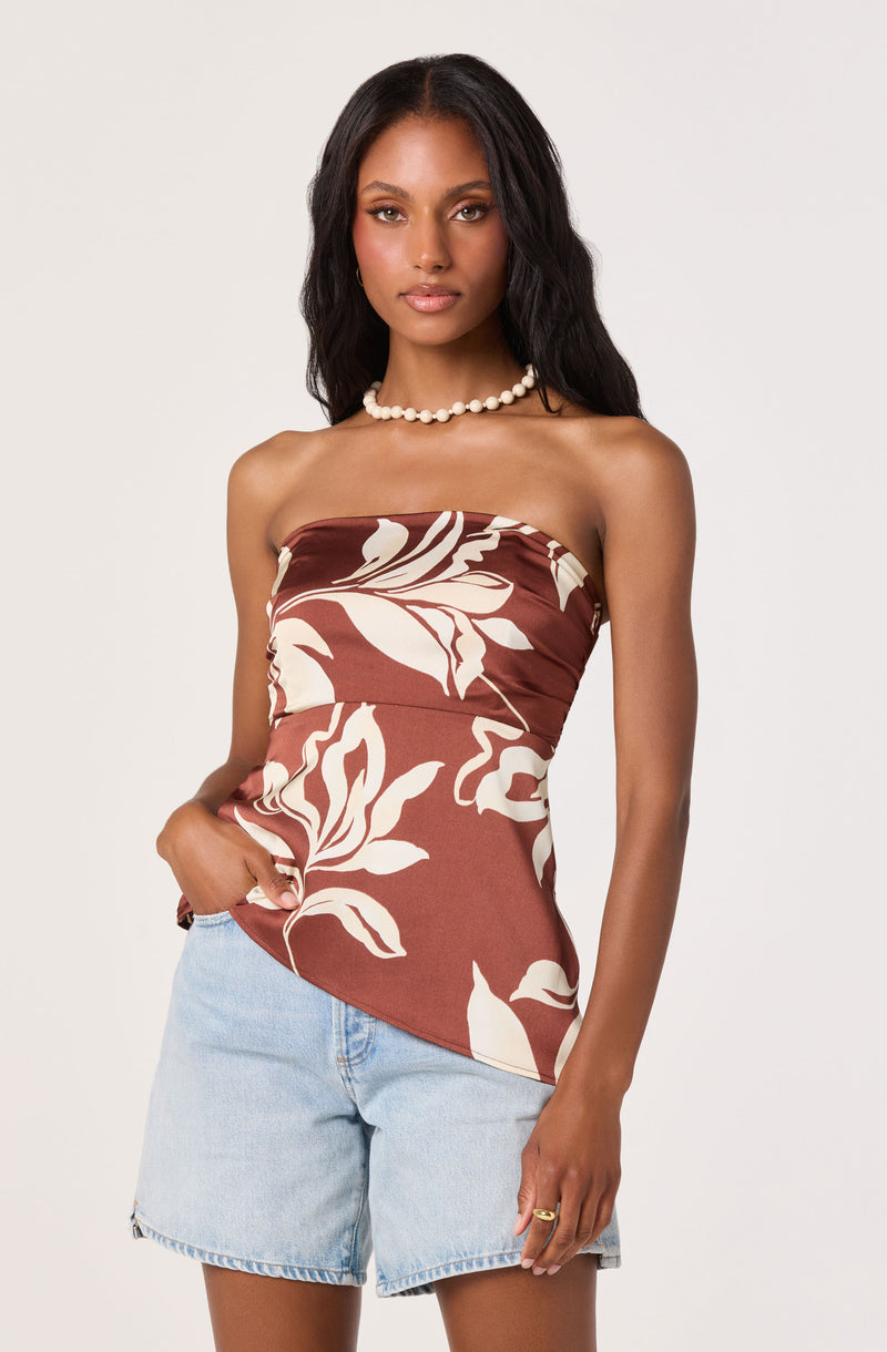 Woman wearing a strapless brown top with large white leaf patterns and light blue denim shorts.