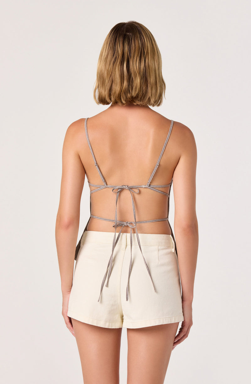Back view of a woman in a spaghetti strap top with string ties and high-waisted beige shorts.