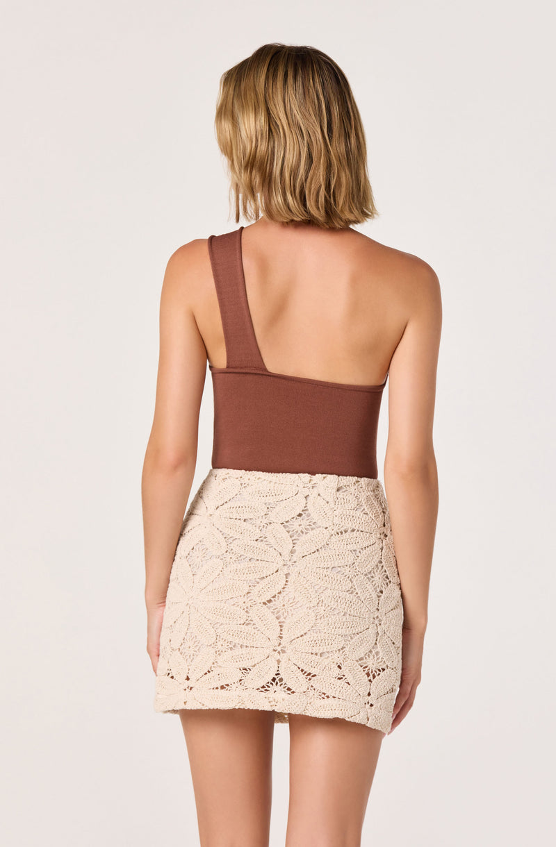 Woman with a one-shoulder brown sleeveless top and a high-waisted cream crochet skirt.