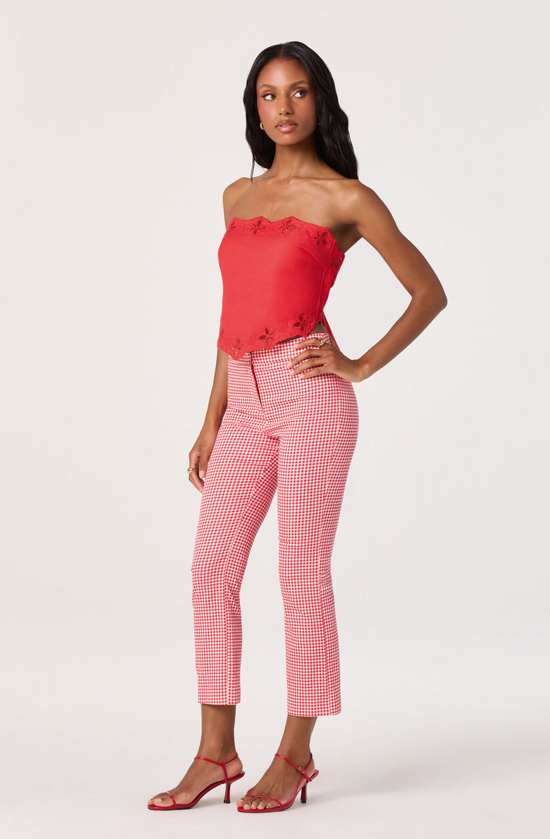 Woman wearing a red strapless top with floral embroidery and pink checkered pants.