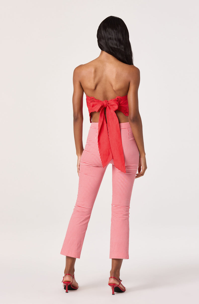 Back view of a woman wearing a red cropped top with a large bow and red-and-white checkered pants.