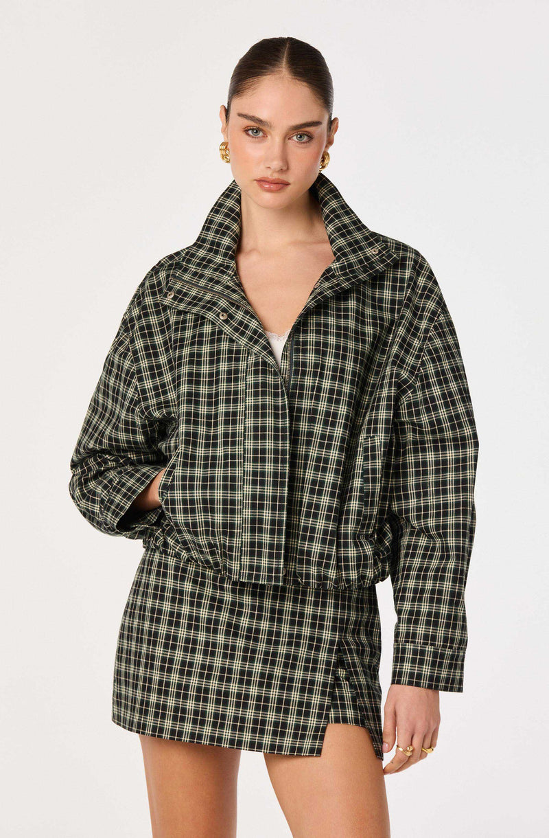 Woman wearing a black and green plaid jacket and matching plaid skirt.