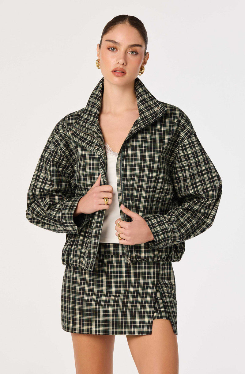 Woman wearing a black and green plaid jacket and matching plaid skirt.