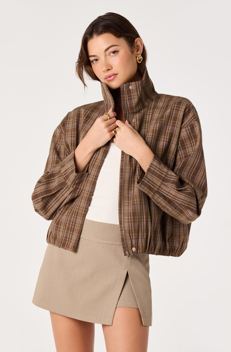 Woman wearing a brown plaid jacket with a high collar and beige skirt.