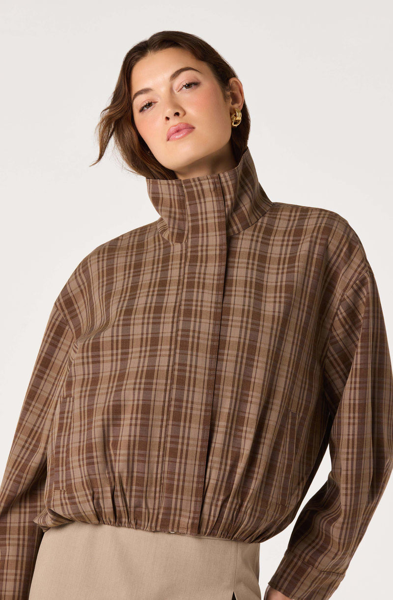 Woman wearing a high-neck, plaid brown and beige jacket with a loose fit.