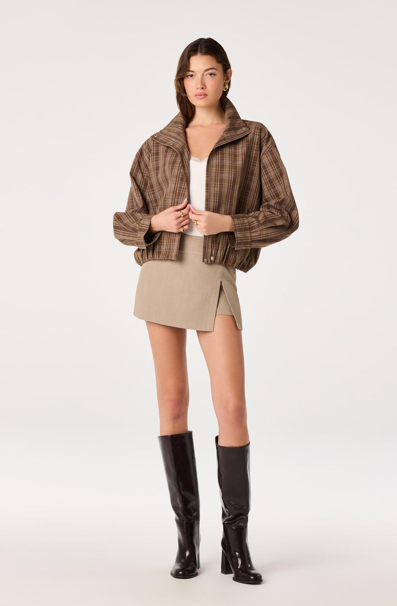 Woman wearing a brown plaid jacket, beige mini skirt, and tall black boots.