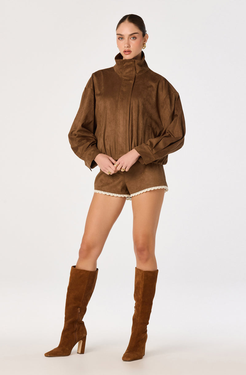 Woman in a brown suede jacket, matching shorts with white trim, and tall brown suede boots.