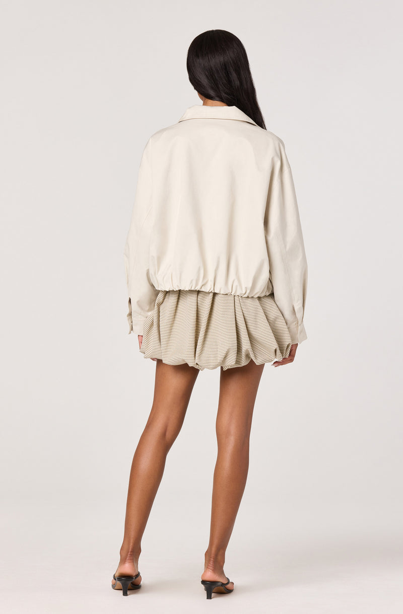 Woman in beige oversized jacket and puffed beige checkered shorts, black heeled sandals.