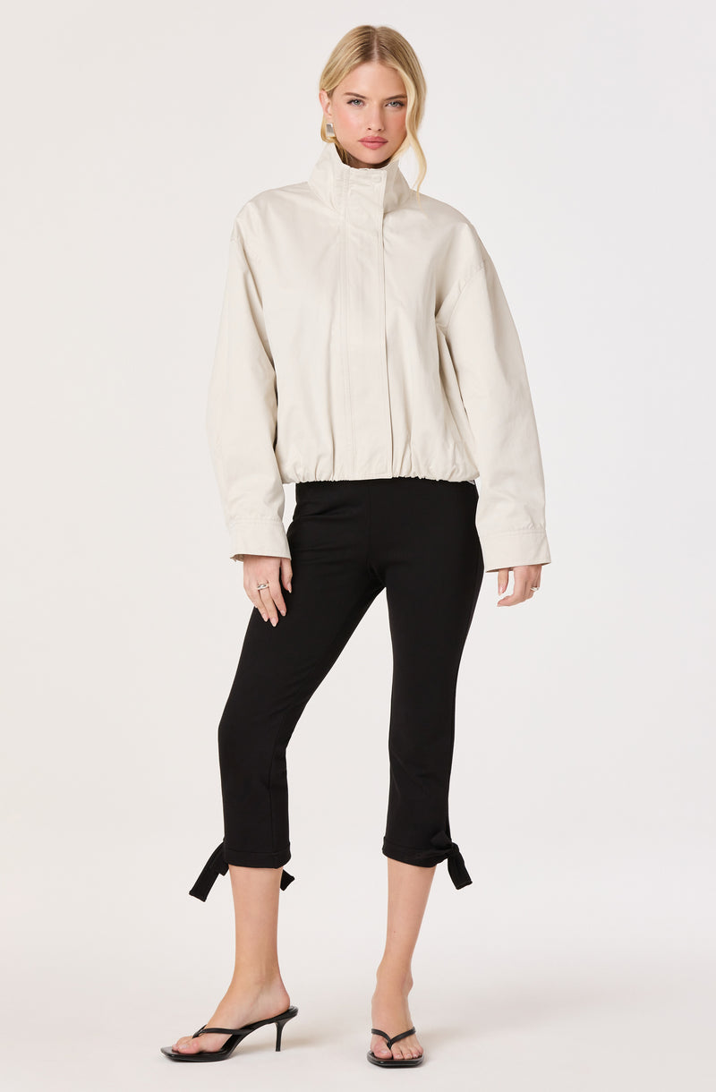 Woman wearing a white cropped jacket with a high collar and black pants with tied cuffs.