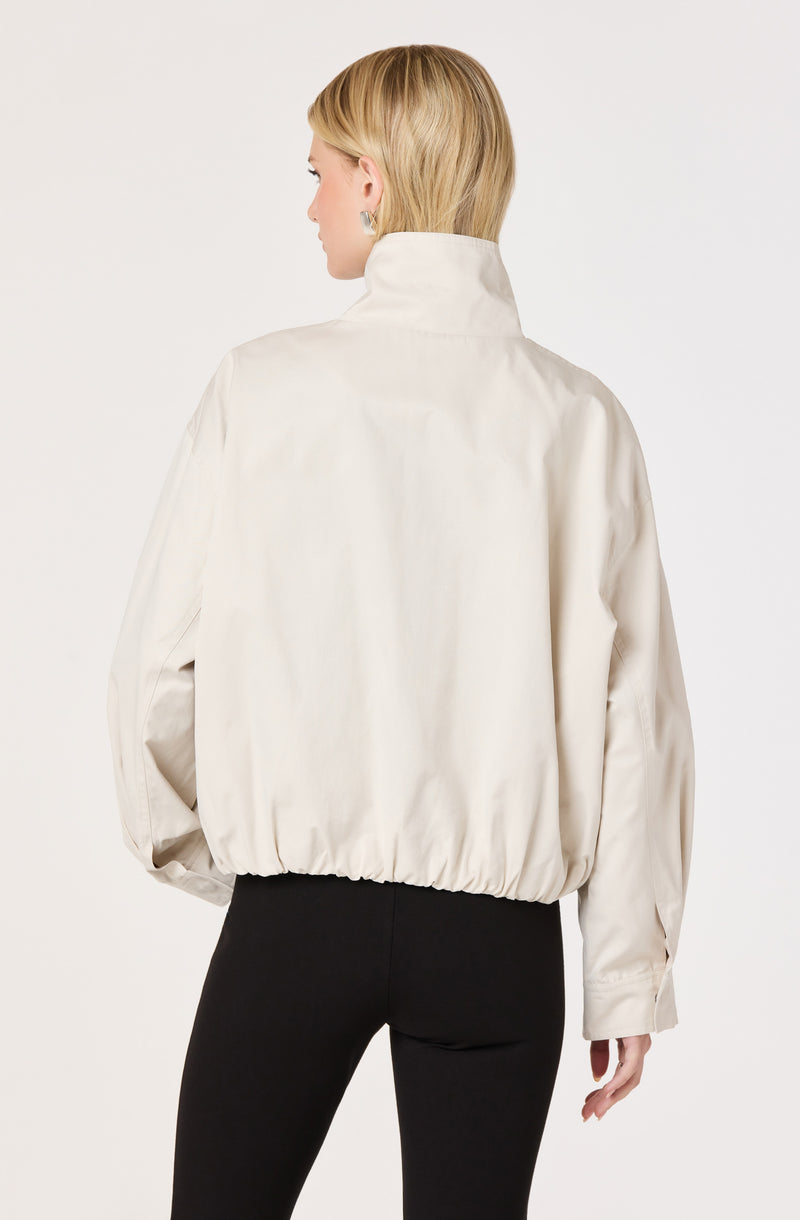 Woman wearing a cream-colored, high-collared, puffy jacket with elastic hem.