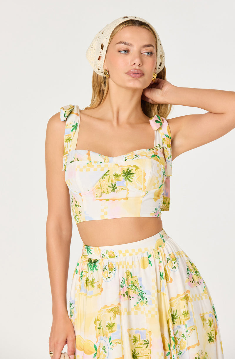 Woman wearing a pastel-colored, tropical print crop top with ruffled shoulder straps and a matching high-waisted skirt.