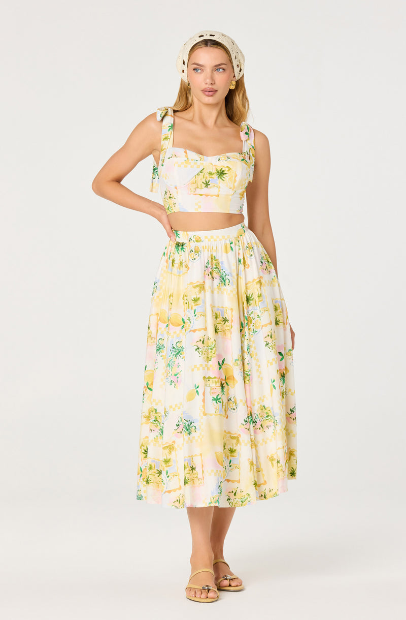 Woman wearing a pastel yellow and pink tropical print sleeveless crop top and long, matching skirt.