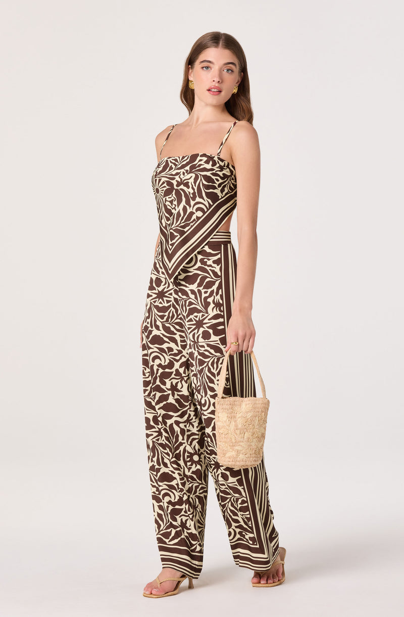 Woman in a matching brown and cream patterned sleeveless top and wide-leg pants, holding a woven bag.