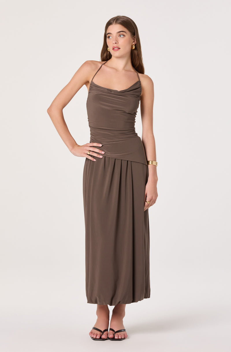 Woman wearing a taupe spaghetti strap maxi dress with ruching at the top and pleats at the bottom.