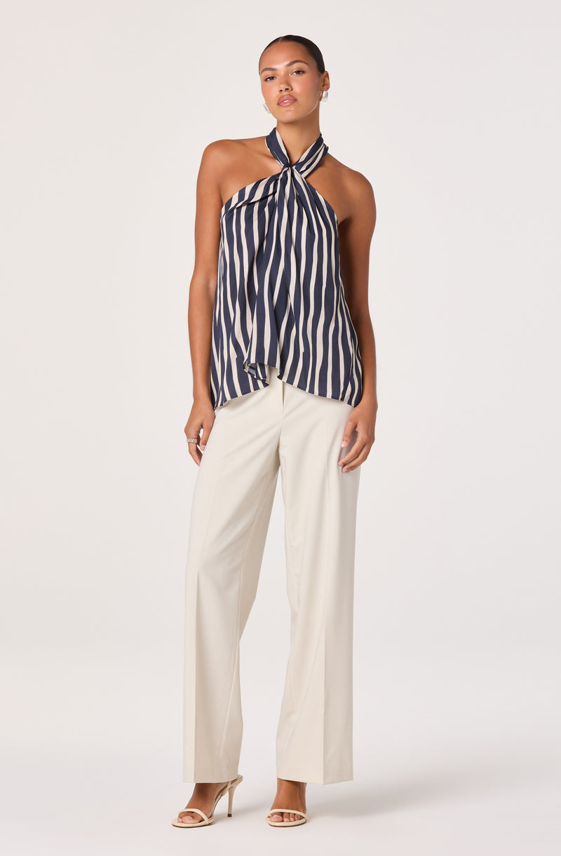 Woman wearing a navy and white striped halter top and cream wide-leg trousers.