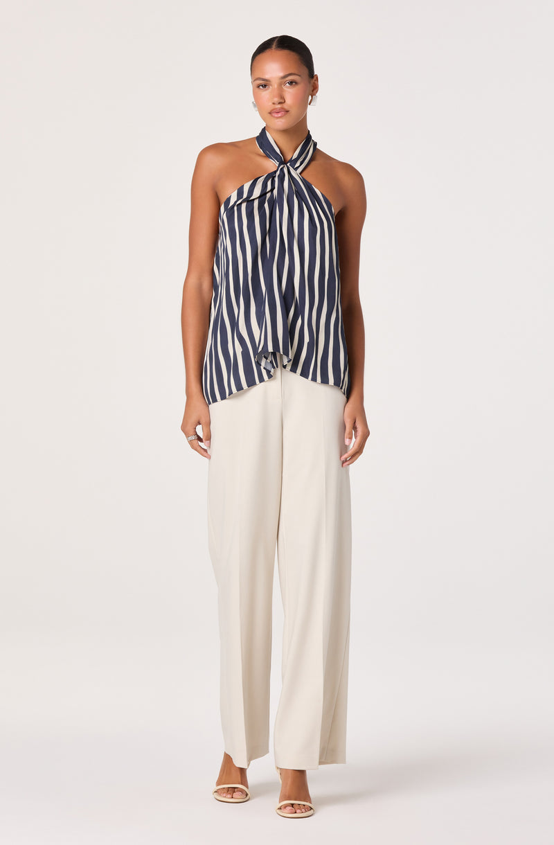Woman wearing a navy and white striped halter top and wide-leg cream pants.
