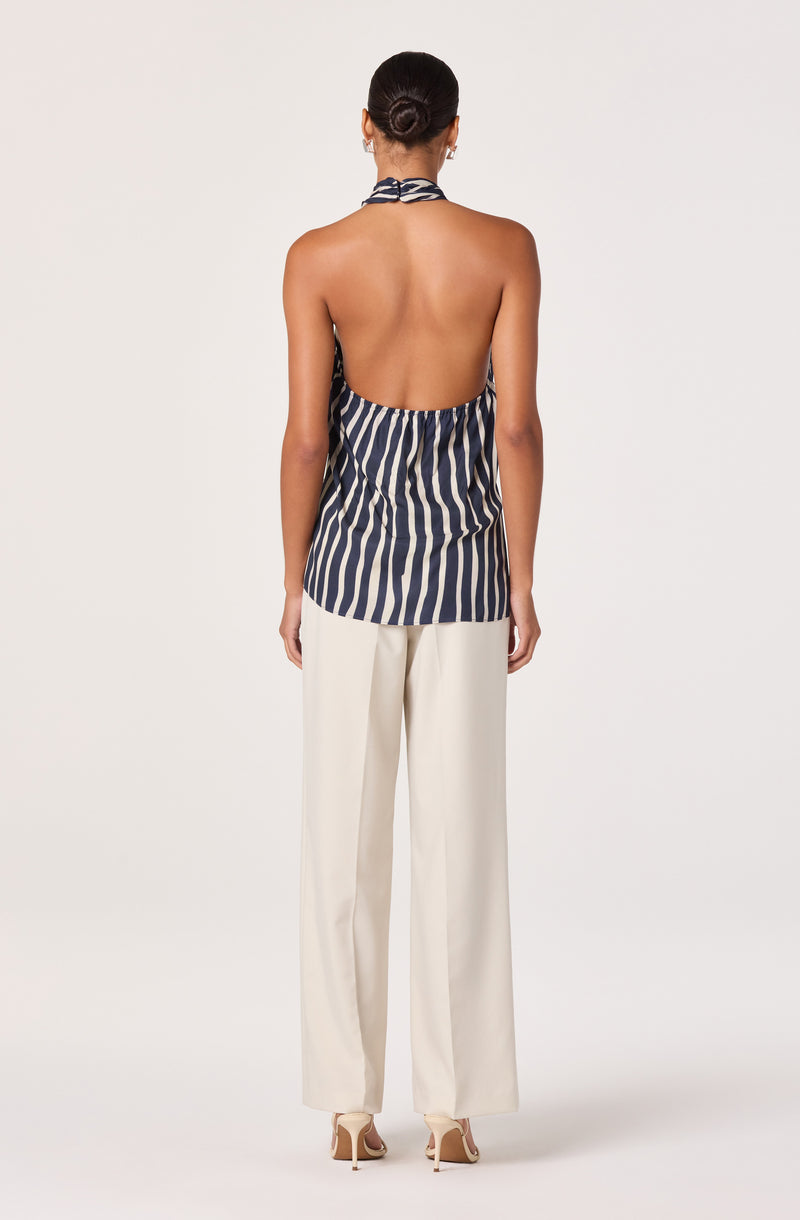 Back view of a woman wearing a halter top with vertical navy and white stripes and white wide-leg pants.