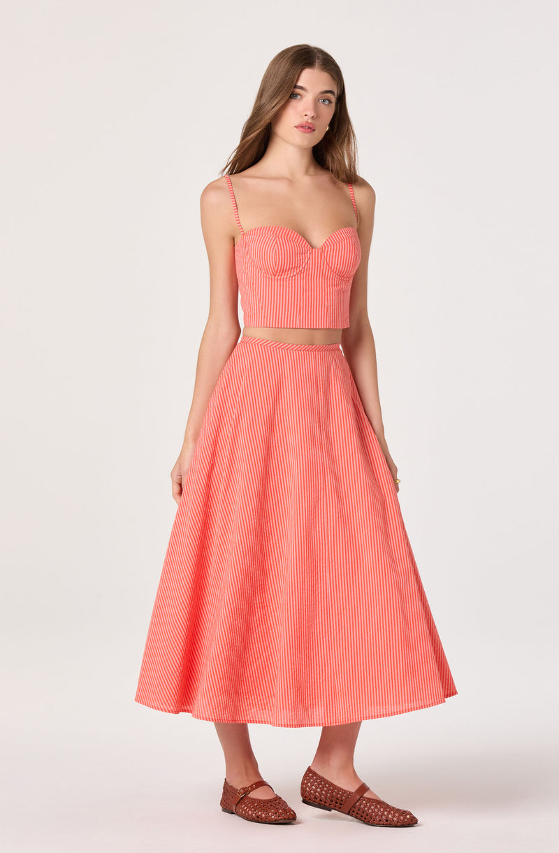 Woman wearing a pink and white vertically striped crop top with thin straps and a matching full-length skirt.