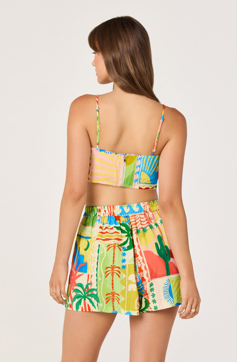 Woman wearing a colorful, tropical-print two-piece outfit with spaghetti straps in front of a plain background.