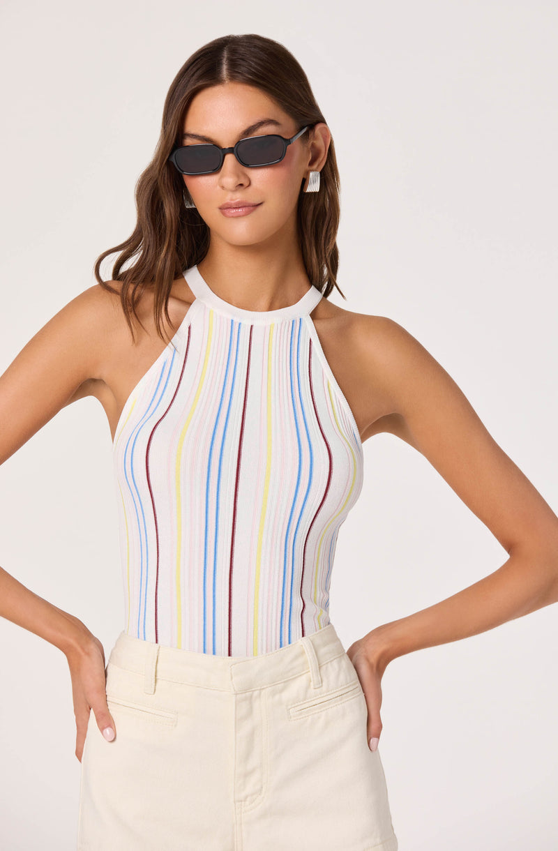 Woman wearing a sleeveless, high-neck top with multicolored vertical stripes and white shorts.