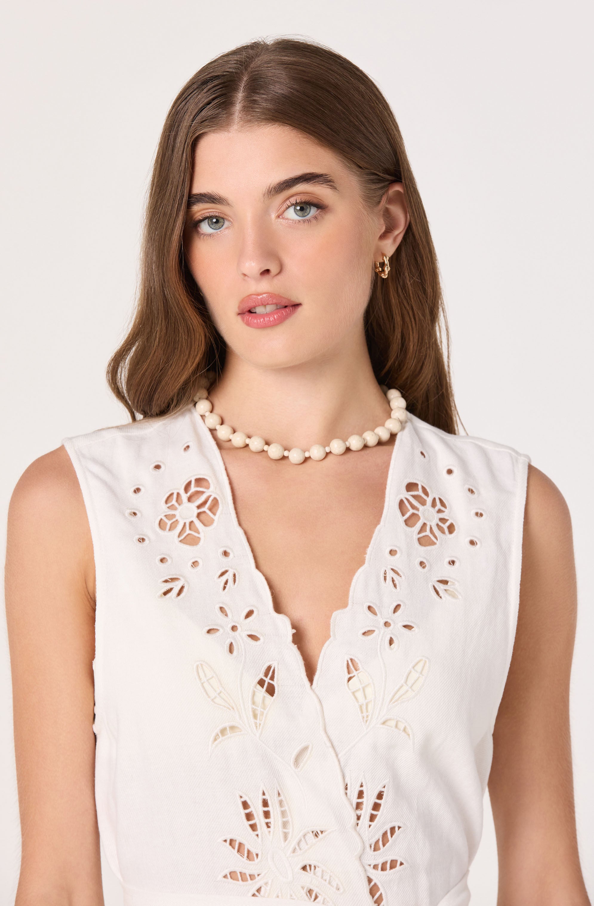 Woman wearing a sleeveless white embroidered top with cut-out floral designs.