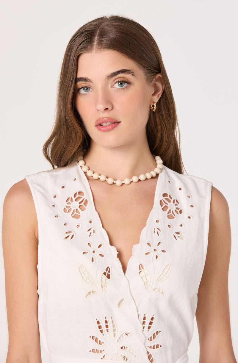 Woman wearing a sleeveless white embroidered top with cut-out floral designs.