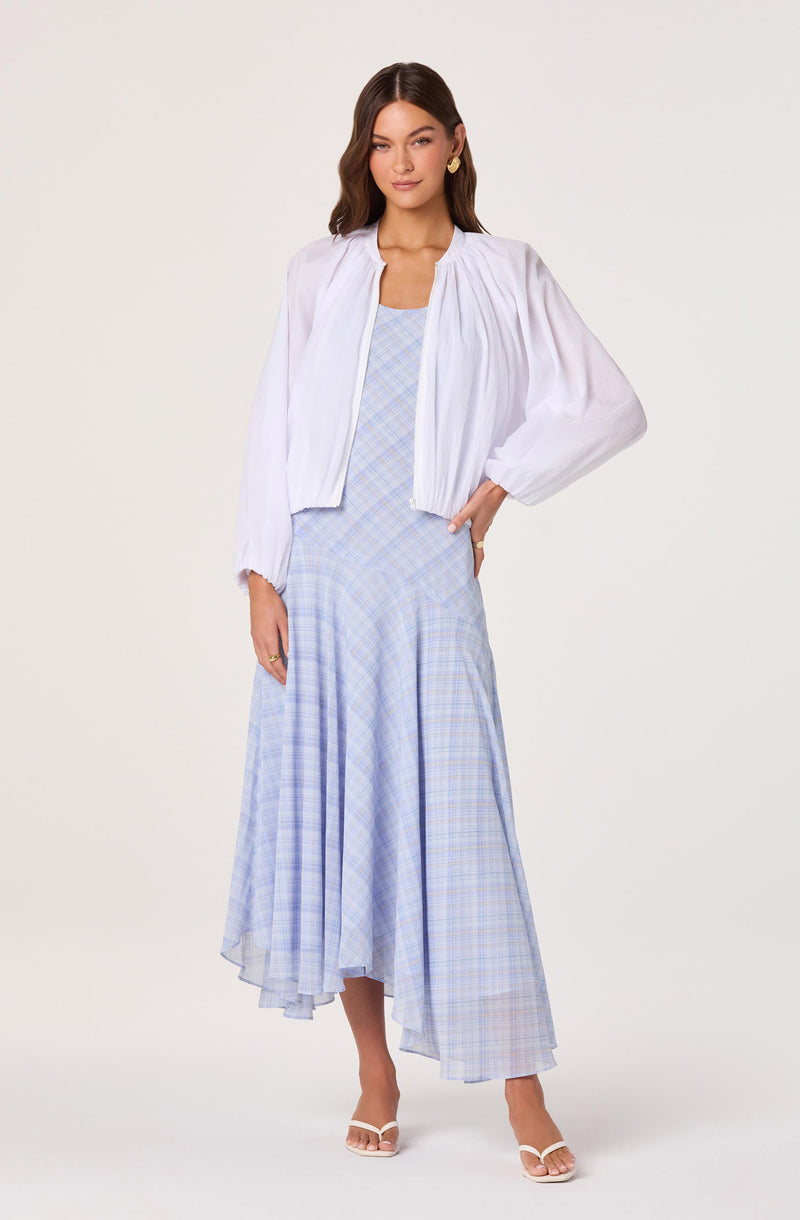 Woman wearing a white puff-sleeve jacket over a light blue plaid dress and white heels.