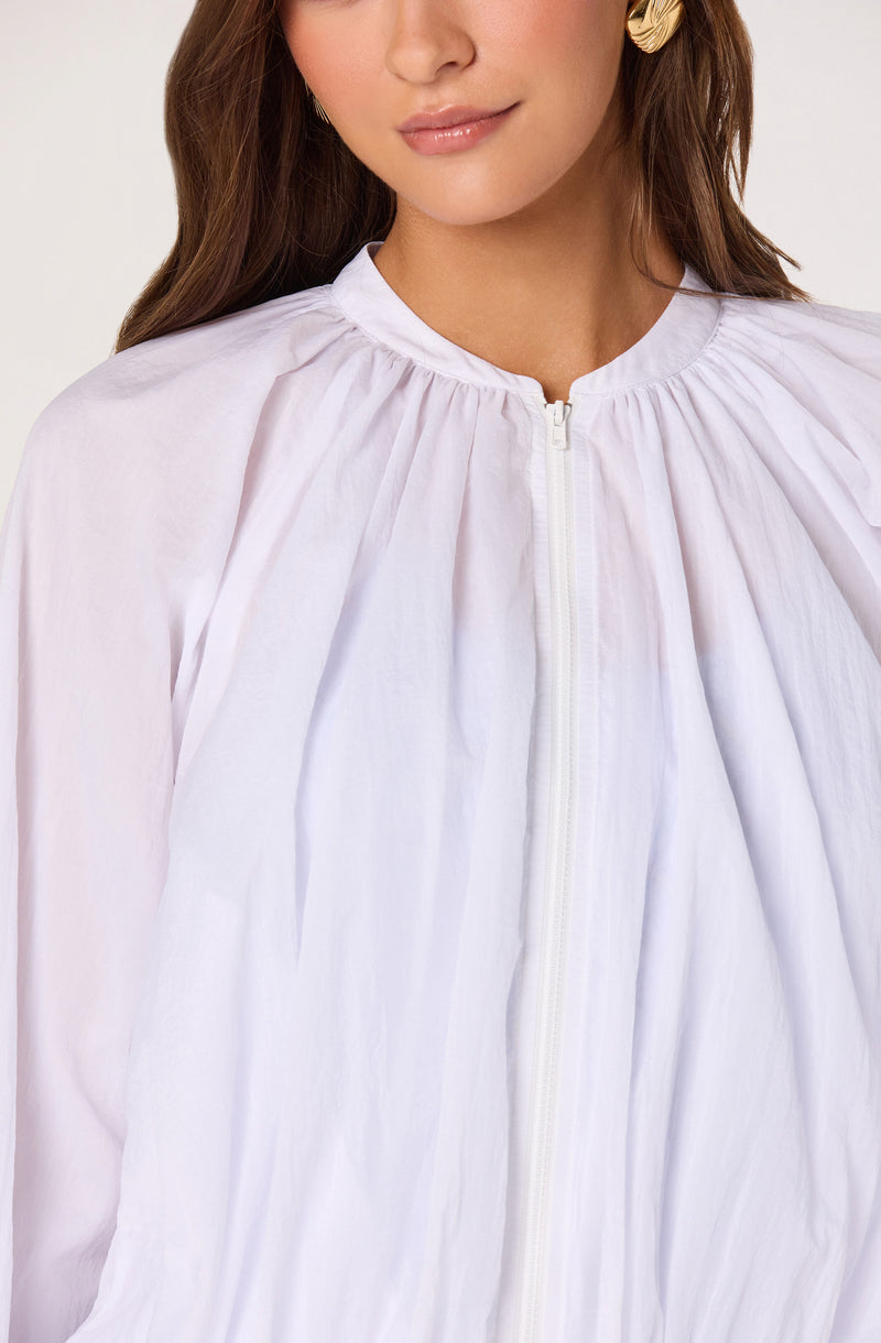 Woman wearing a white pleated zip-up blouse with a round neckline.