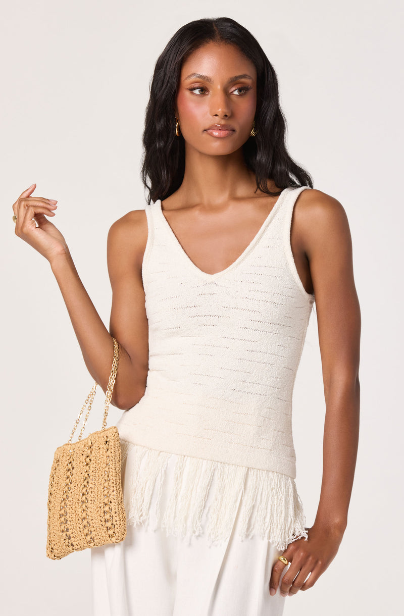 Woman wearing a sleeveless, V-neck, white textured top with a fringed hem.