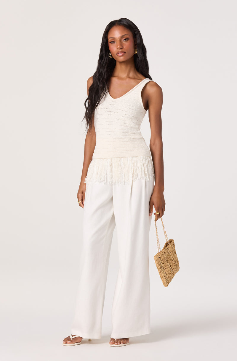 Cream sleeveless knit top with fringe hem, paired with wide-leg white pants and beige open-toe heels.