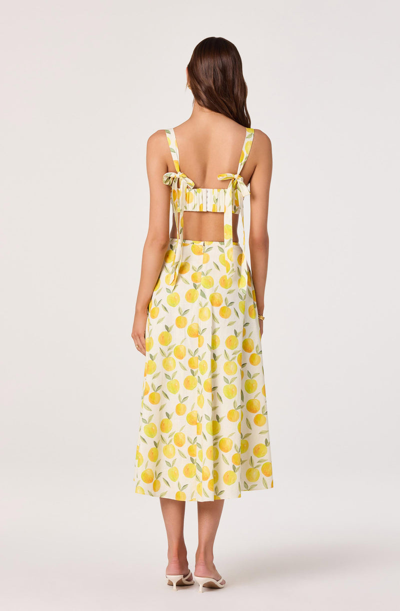Back view of a woman wearing a yellow and white lemon print dress with shoulder bows and an open back.
