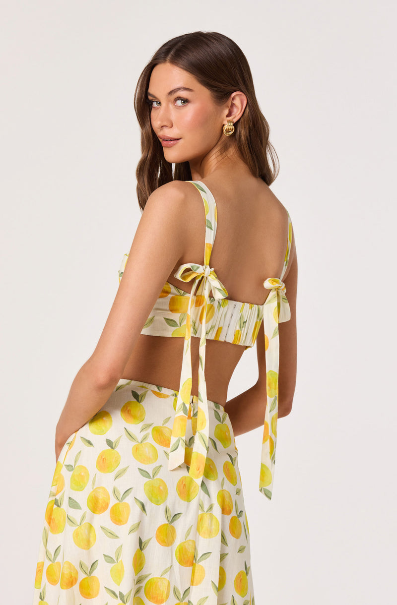 Woman in a yellow citrus print crop top and matching wide-leg skirt, both with bow-tie straps.