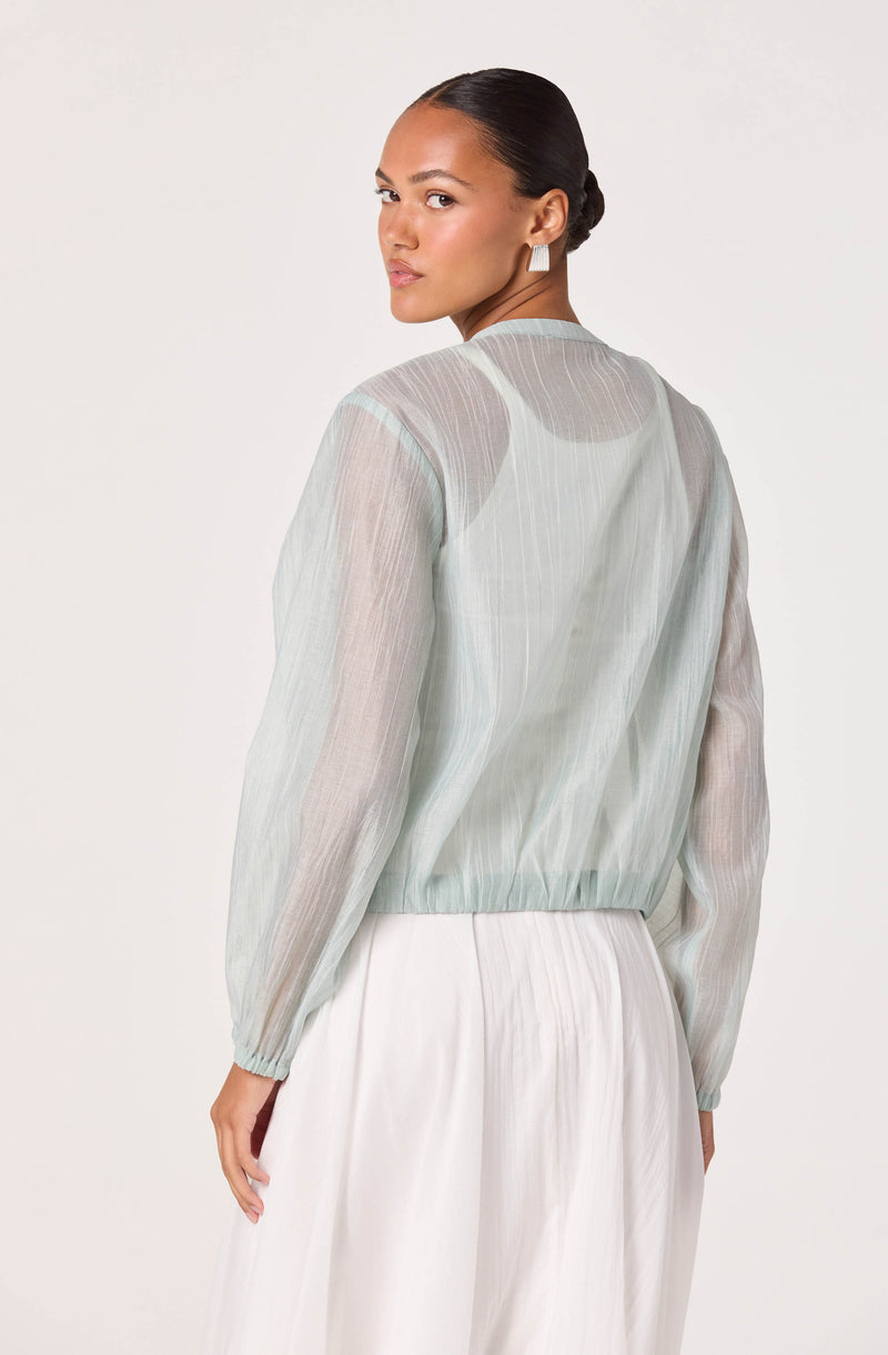 Woman wearing a sheer, light pastel-colored long-sleeve blouse with elastic hem, and white skirt.