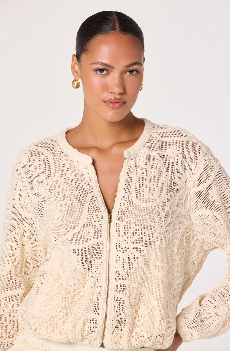 Woman wearing a cream-colored, floral lace zip-up sweater.