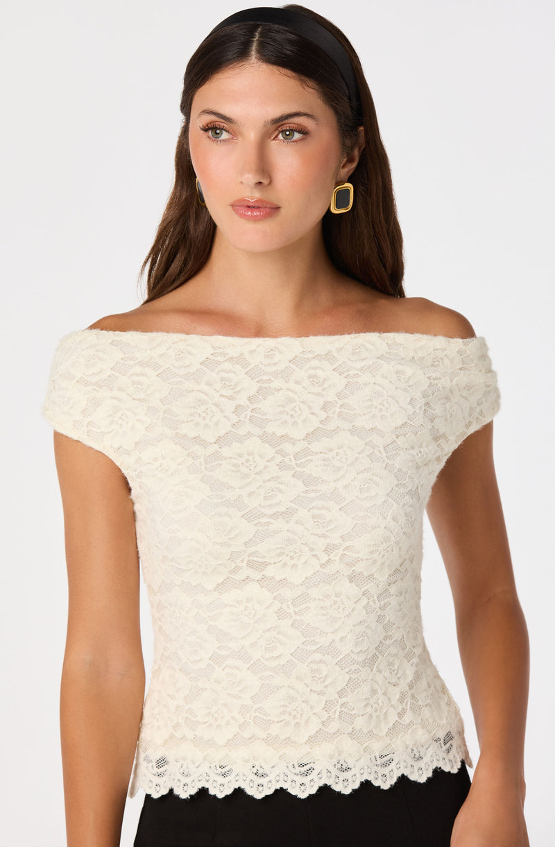 Woman in off-shoulder white lace top with scalloped hem, gold geometric earrings, black headband.