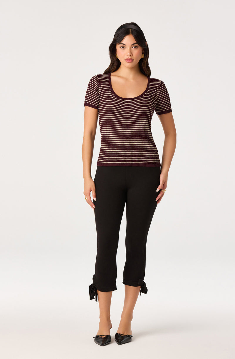 Woman wearing a fitted, short-sleeve, striped top and black cropped pants with tied cuffs.