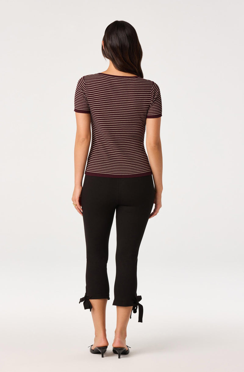 Woman wearing a short-sleeve, striped maroon and beige top and black cropped pants with bow ties at the cuffs.