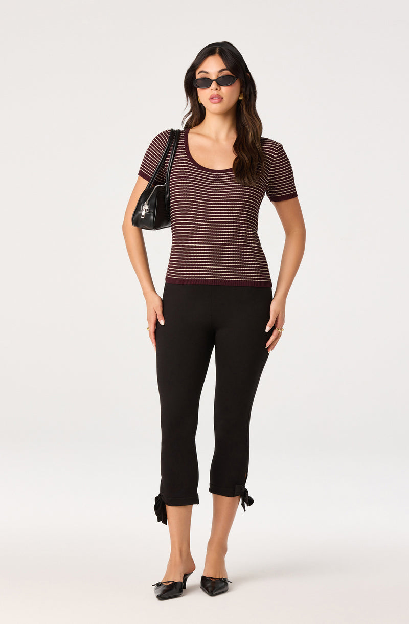  woman wearing a short-sleeve striped top, black cropped pants with tied hems, black pointed shoes, and black sunglasses, carrying a black shoulder bag
