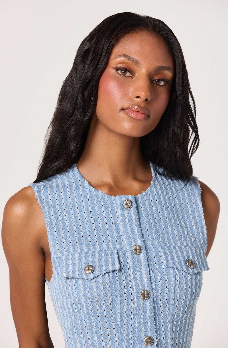 Woman wearing a sleeveless, light blue textured fabric top with silver buttons.