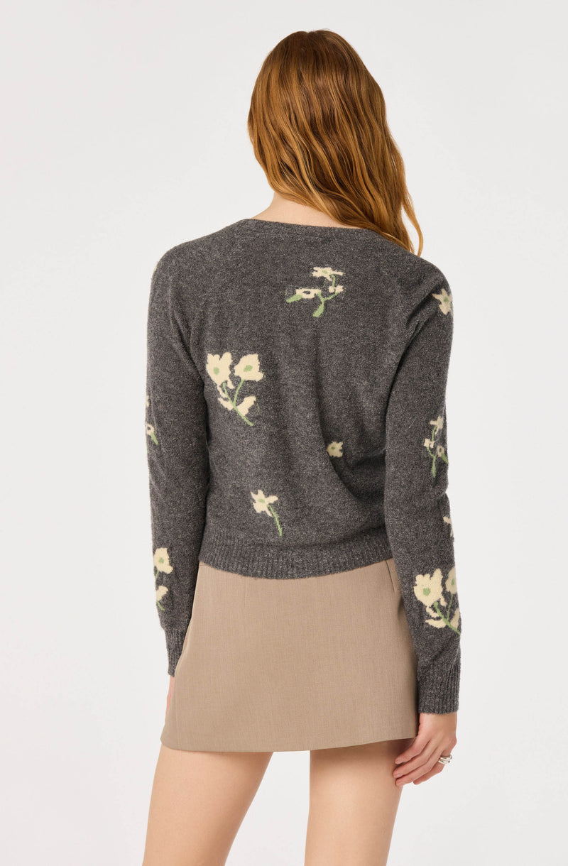 Woman wearing a gray cardigan with floral patterns and a beige skirt.