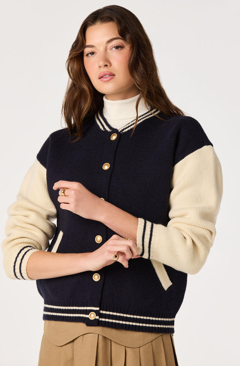 Young woman in navy and cream varsity jacket with striped cuffs and gold buttons.
