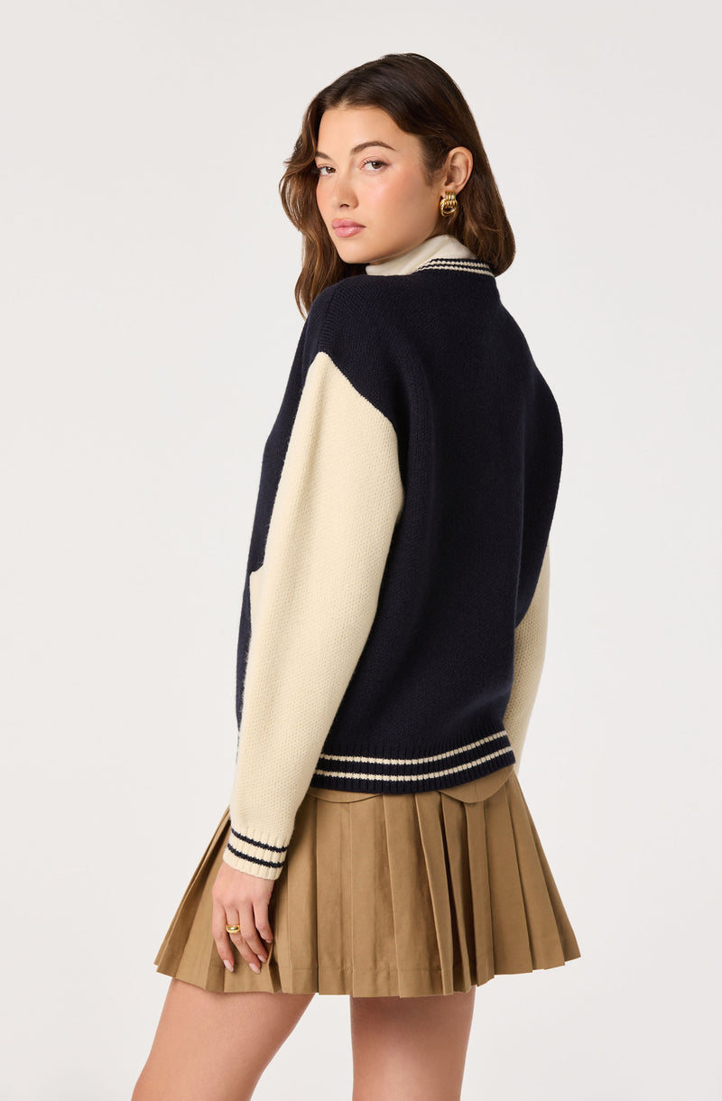 Woman wearing a navy and cream color-block sweater with striped cuffs and a beige pleated skirt.