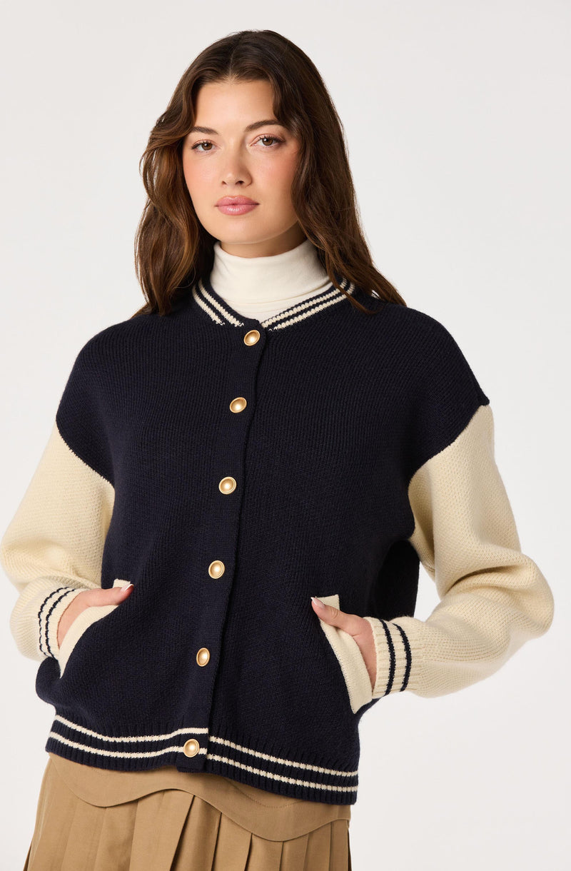 Woman wearing a navy and cream varsity-style sweater with striped trim and buttons.