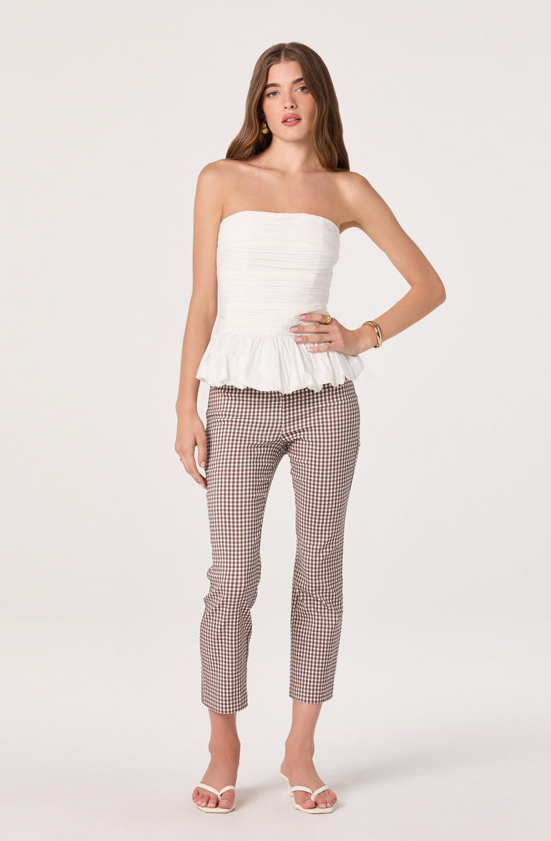 Woman wearing a strapless white ruffled top and gingham patterned pants.