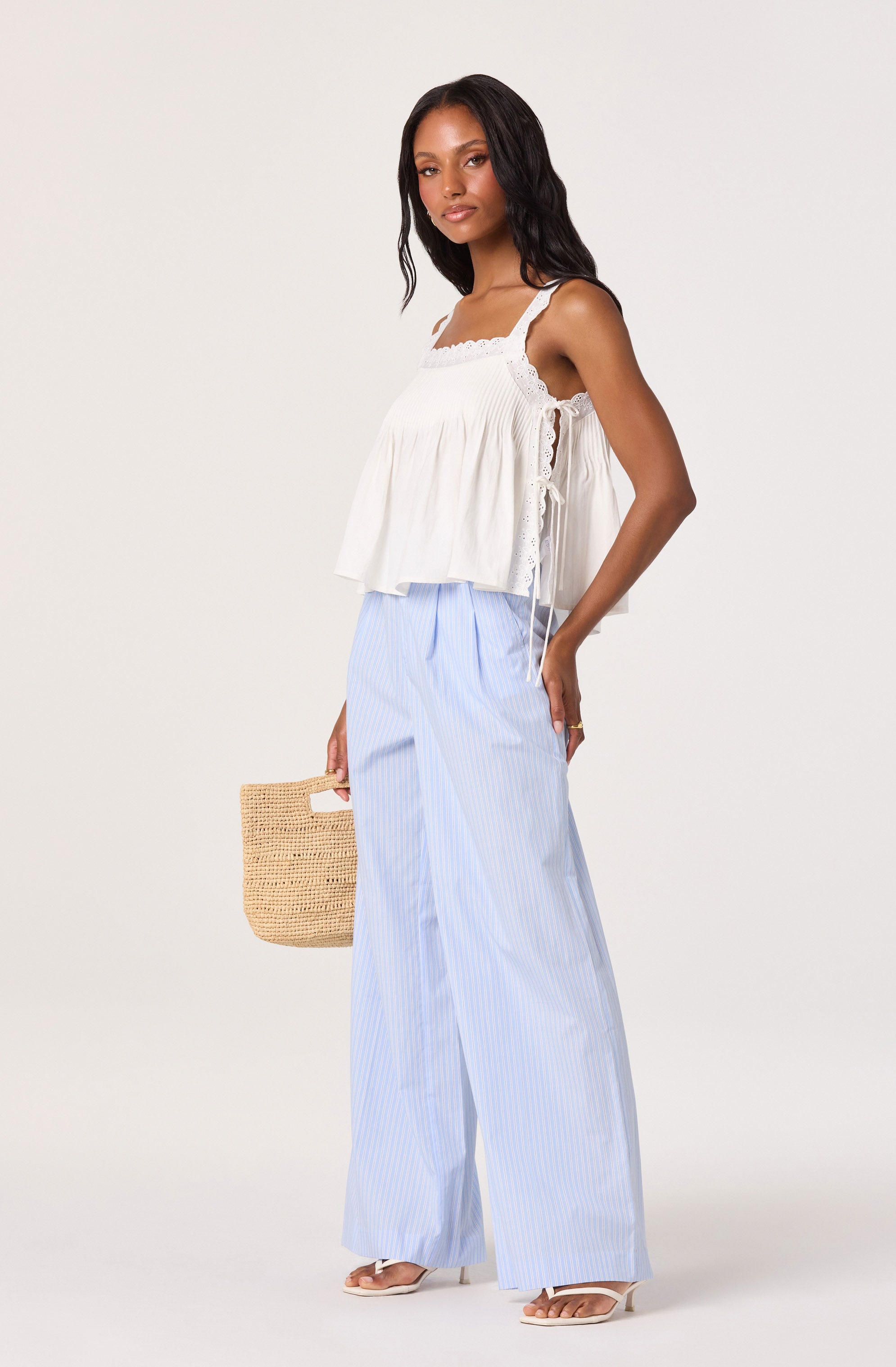 Woman wearing a white sleeveless, ruffled top with lace details, paired with light blue and white striped wide-leg pants.