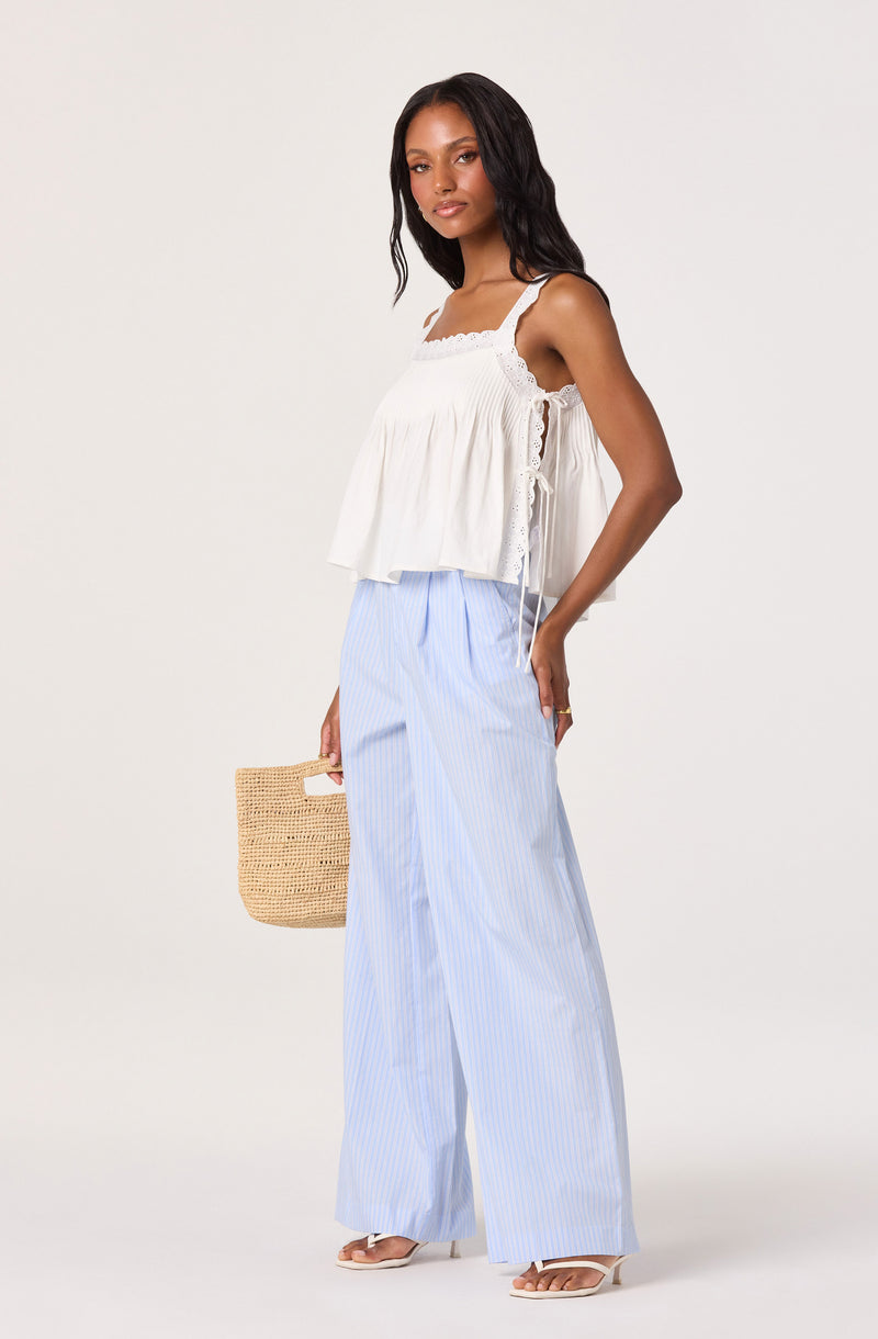 Woman wearing a white sleeveless, ruffled top with lace details, paired with light blue and white striped wide-leg pants.