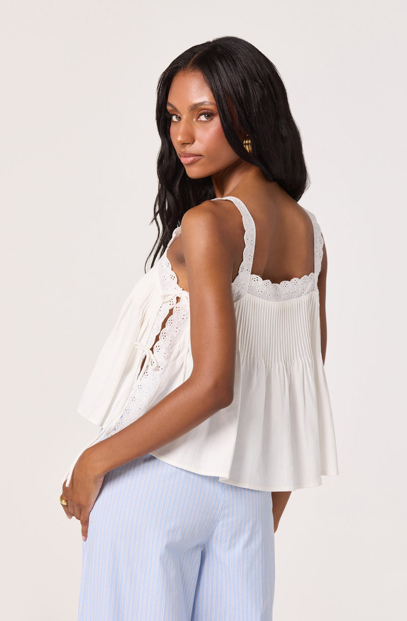 Woman wearing a white sleeveless top with lace straps and pleated details, paired with light blue and white striped pants.