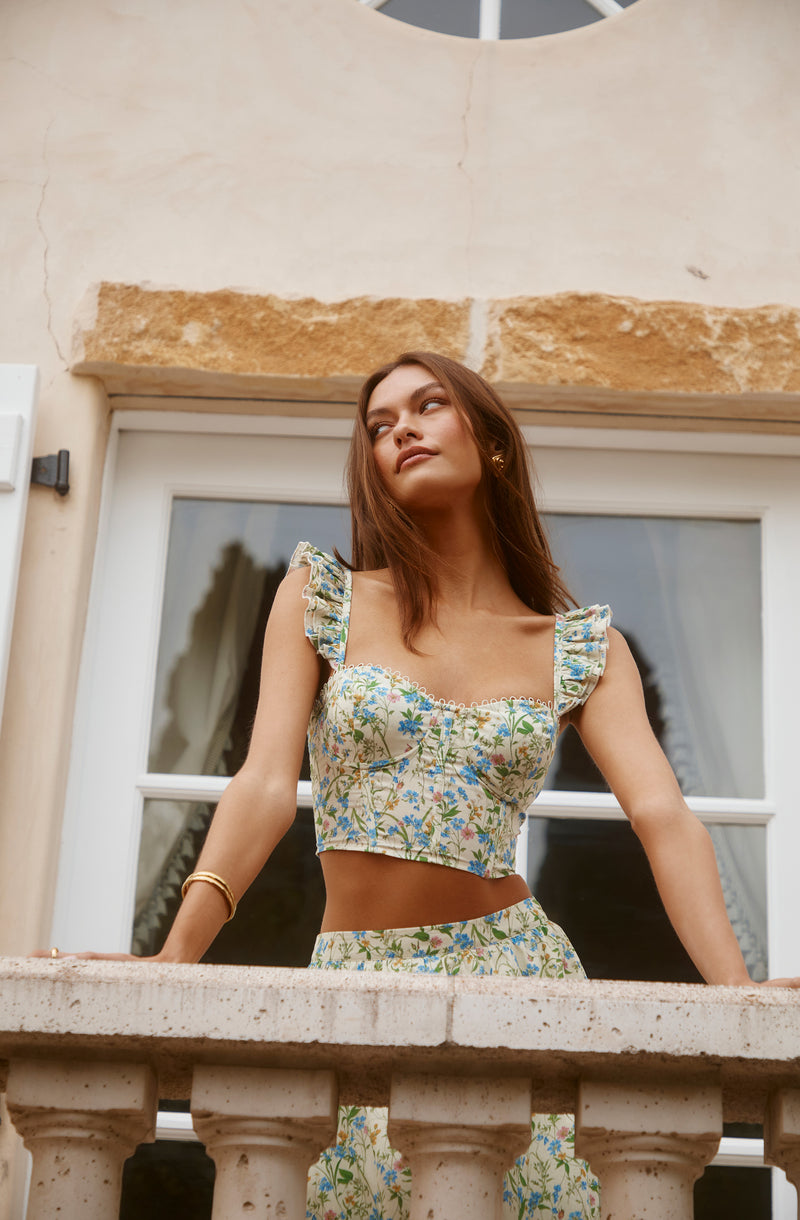 Young woman in a floral crop top with ruffled sleeves and matching skirt, standing outdoors.