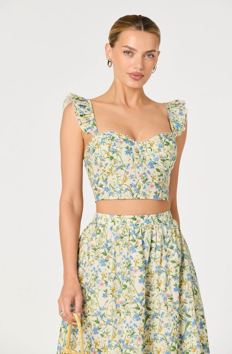 Woman wearing a floral crop top with ruffled shoulder straps and a matching high-waisted skirt.