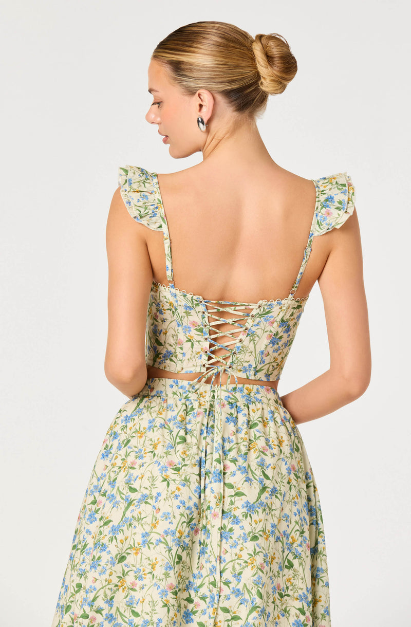 Back view of a woman wearing a floral dress with ruffled shoulder straps and a laced-up back.